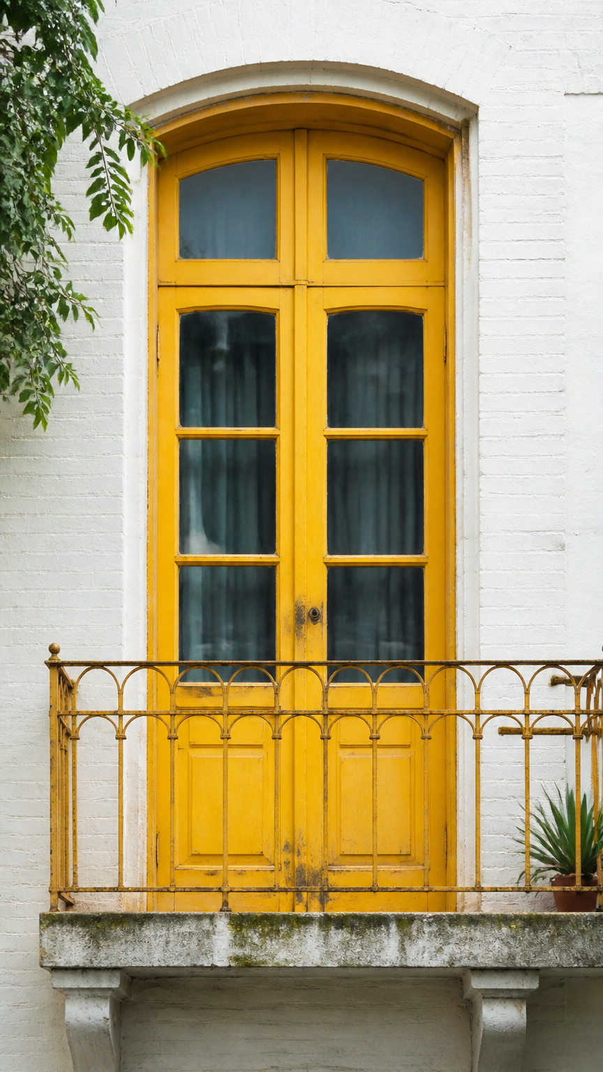 A high-end photograph of a vintage wooden balcony door painted in a vibrant mustard yellow, set against neutral white...